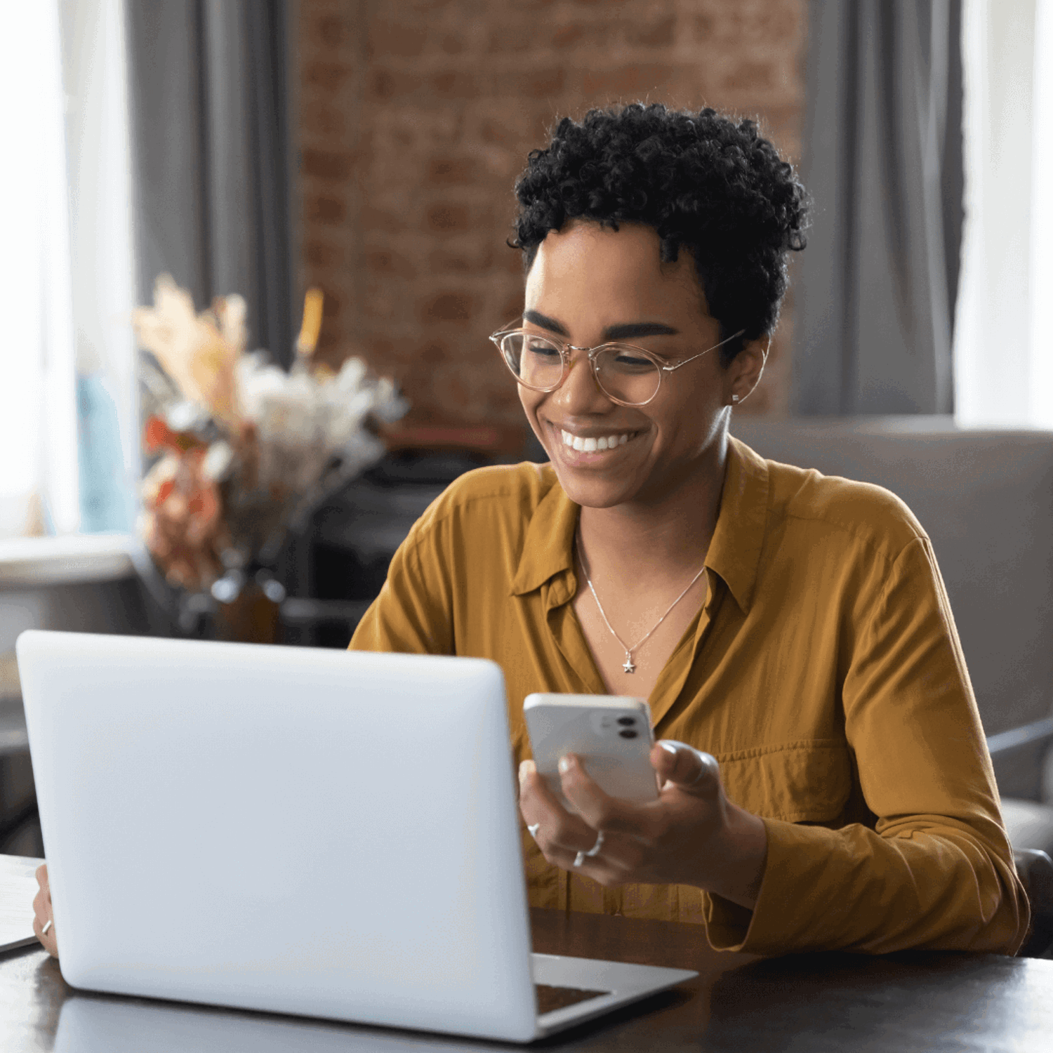 Smiling person looking at a laptop, holding a mobile phone